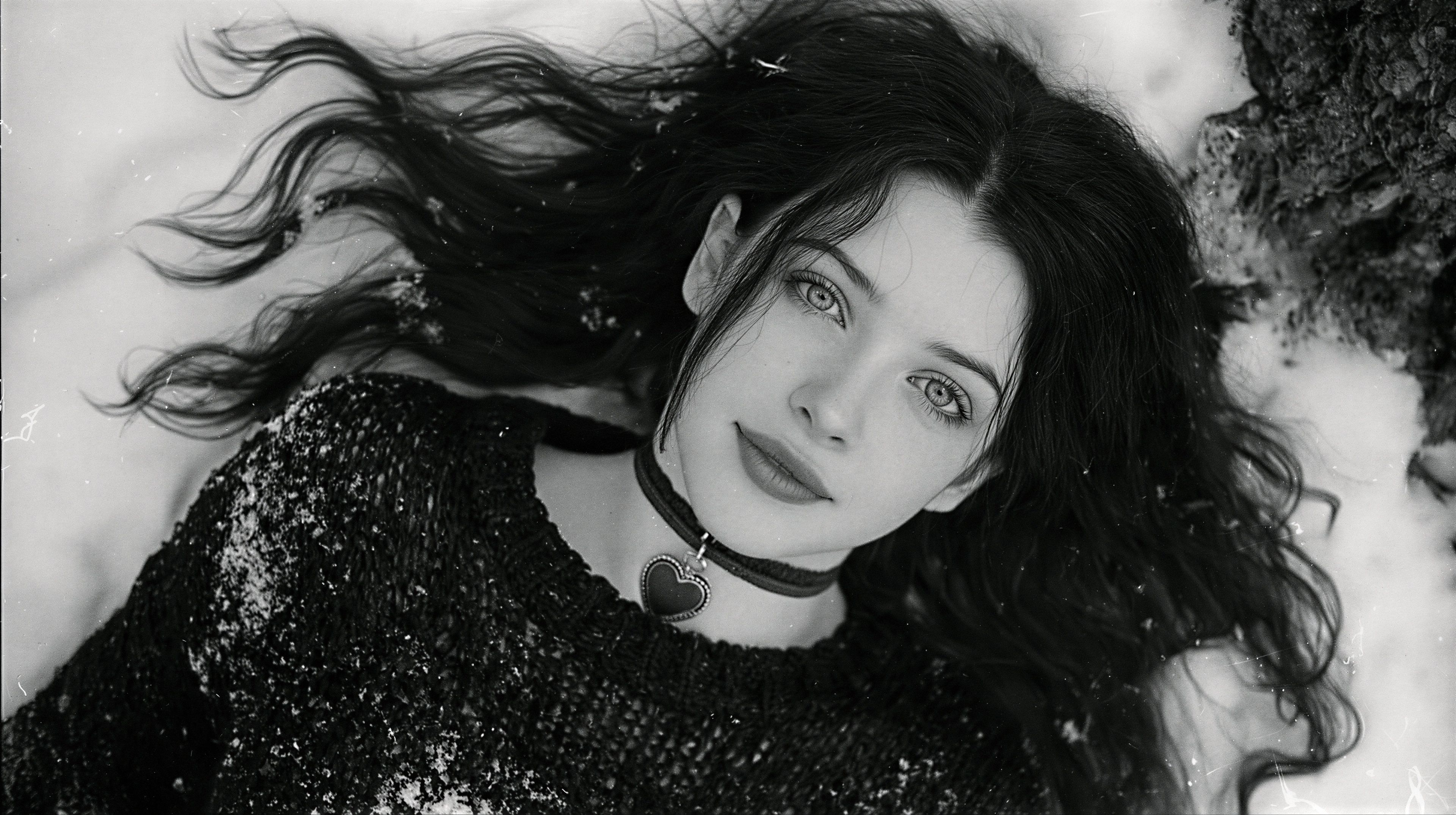 A young woman lies gracefully in the snow, her gaze meeting the viewer's with a captivating intensity.