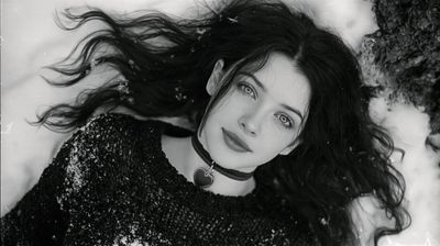 A young woman lies gracefully in the snow, her gaze meeting the viewer's with a captivating intensity.