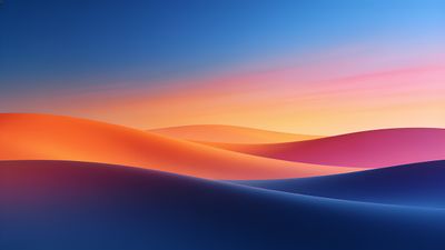 A vibrant sunset casts warm hues of orange, pink, and purple over gently rolling sand dunes, creating a serene and tranquil atmosphere against a clear blue sky.