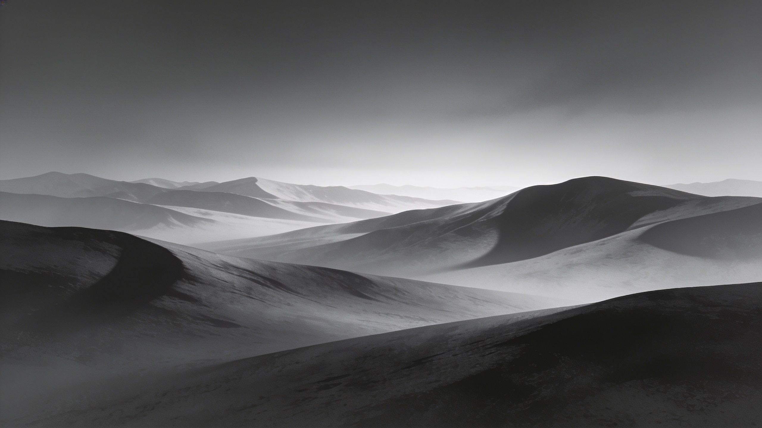 A serene black and white landscape featuring rolling mountain ranges under a soft, misty sky, creating a tranquil and timeless atmosphere.