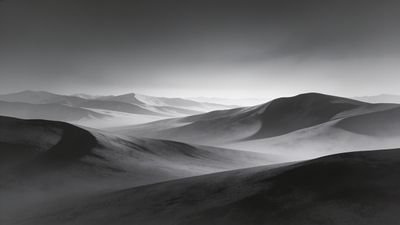 A serene black and white landscape featuring rolling mountain ranges under a soft, misty sky, creating a tranquil and timeless atmosphere.