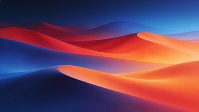 A vibrant sunset casts a warm glow over undulating sand dunes in vivid shades of orange, red, and blue, creating a surreal and tranquil landscape. The smooth curves of the dunes and the rich colors evoke a sense of calm and wonder.