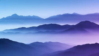 A tranquil scene of misty mountain ranges layered in soft blue and purple hues at dawn, creating a peaceful and ethereal atmosphere. The gentle gradient of colors and the mist enveloping the peaks evoke a sense of calm and serenity.