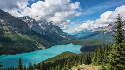 A serene mountain landscape featuring a turquoise lake surrounded by lush green forests and towering, rugged peaks under a partly cloudy blue sky, creating a tranquil and majestic atmosphere.