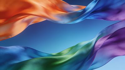 Colorful silk ribbons in shades of orange, blue, green, and purple gracefully flow against a clear blue sky, creating a vibrant and serene atmosphere.