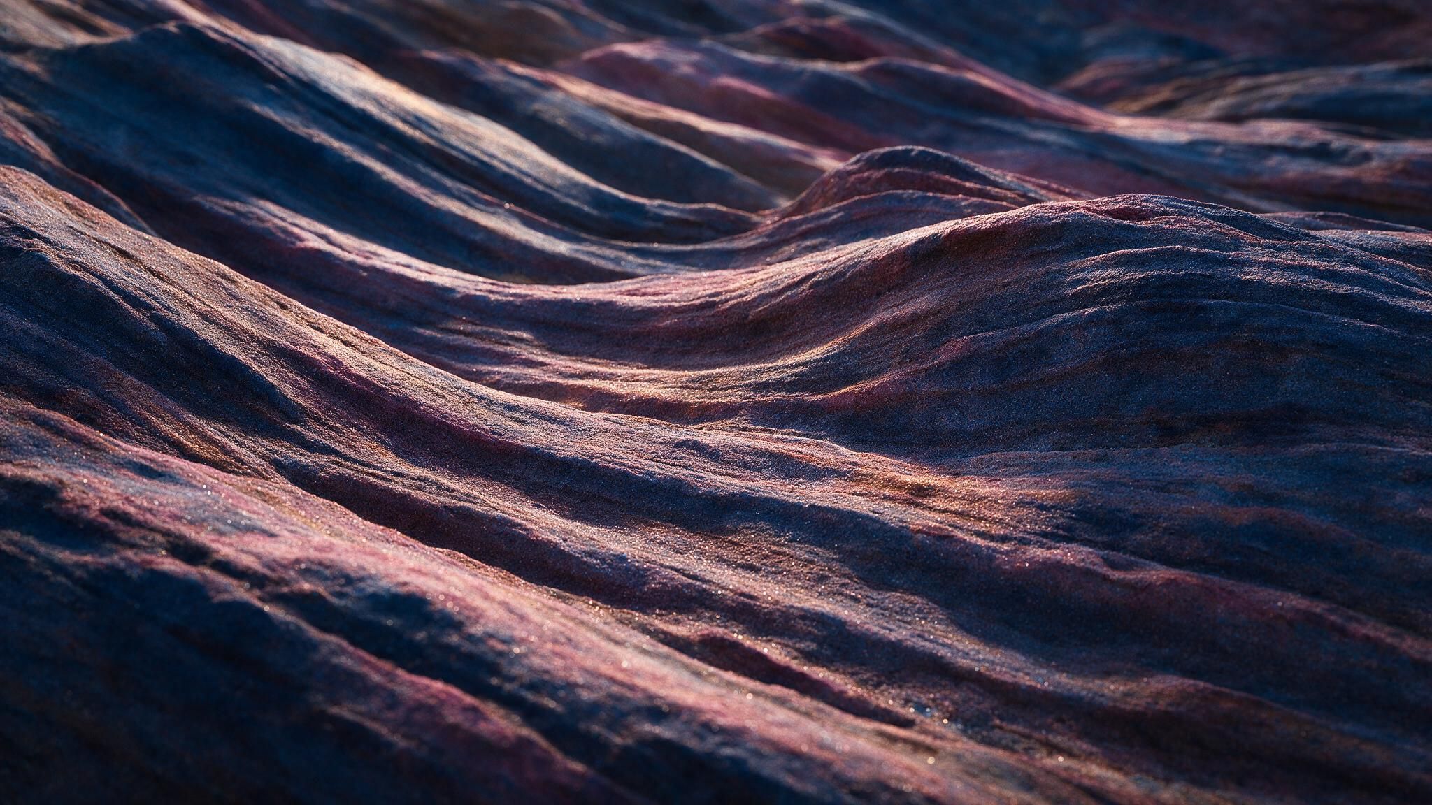 Soft twilight light gleams across close-up sand ripples, their blue-violet and rosy grains glittering like miniature waves on a serene, empty shore. The rich 4K HD detail and gentle shadows evoke a calm, otherworldly mood.