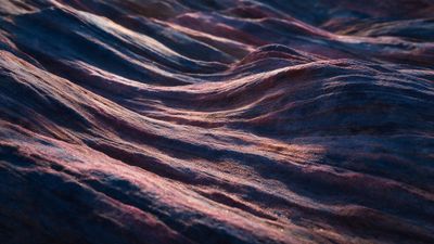 Soft twilight light gleams across close-up sand ripples, their blue-violet and rosy grains glittering like miniature waves on a serene, empty shore. The rich 4K HD detail and gentle shadows evoke a calm, otherworldly mood.