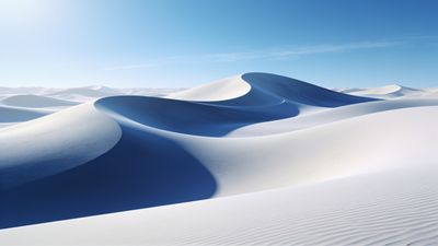 A vast expanse of smooth, blue-tinted desert dunes is bathed in the soft glow of sunrise, creating a tranquil and serene atmosphere under a clear blue sky.