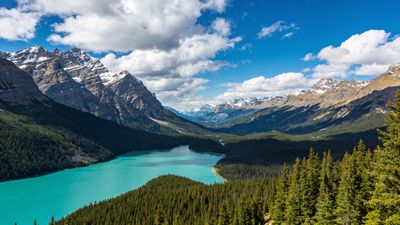 A serene turquoise lake is nestled among lush evergreen forests and towering snow-capped mountains under a clear blue sky, creating a tranquil and majestic atmosphere.