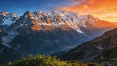 A breathtaking view of snow-capped mountains bathed in the warm, golden hues of a sunset, with a lush green valley below, creating a serene and majestic atmosphere.