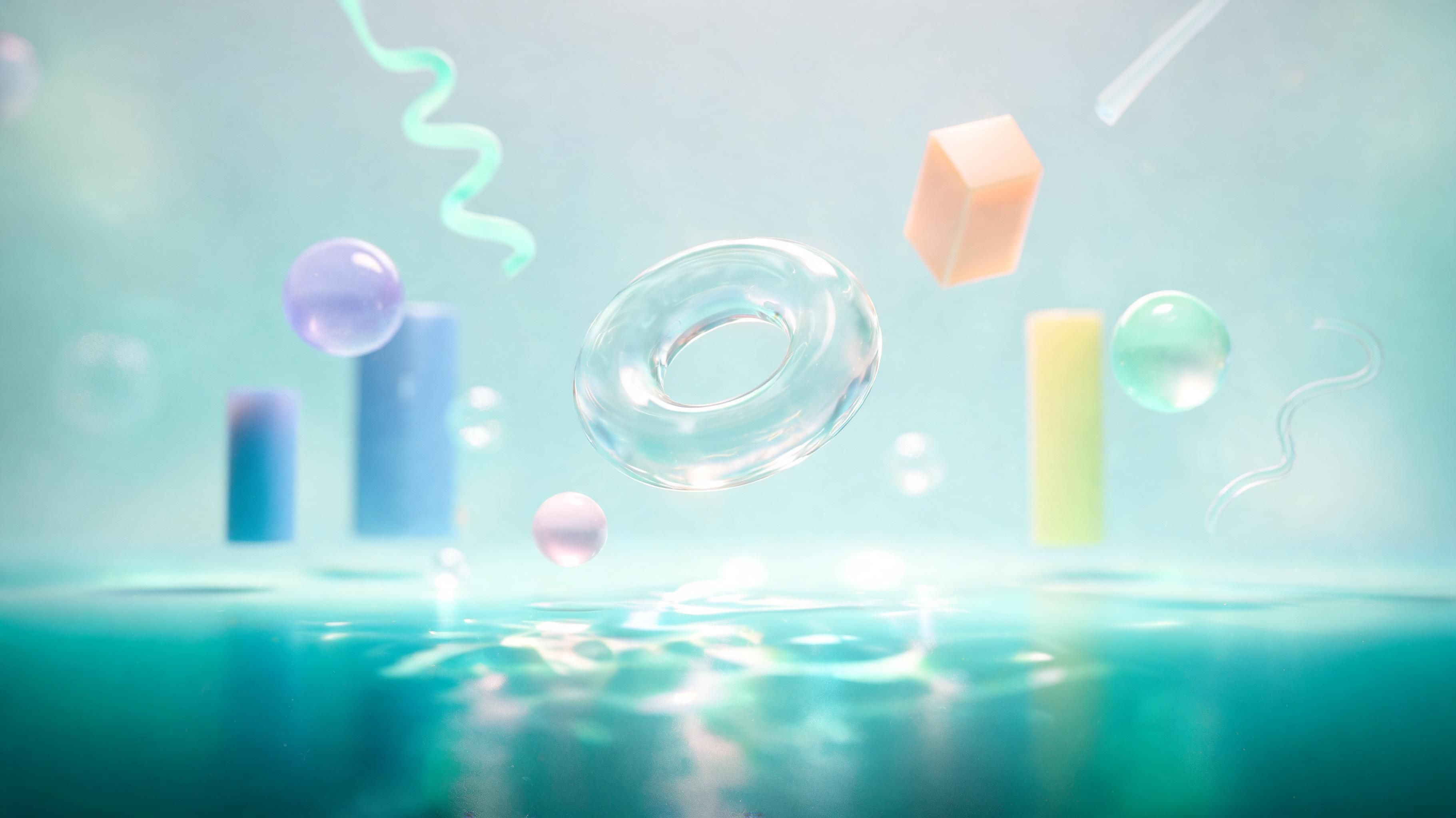 Glossy pastel spheres, cylinders, a translucent doughnut ring, and other abstract shapes hover above a softly rippling turquoise water surface, lit by gentle, diffused light. The airy composition and muted colours create a calm, dreamlike mood.