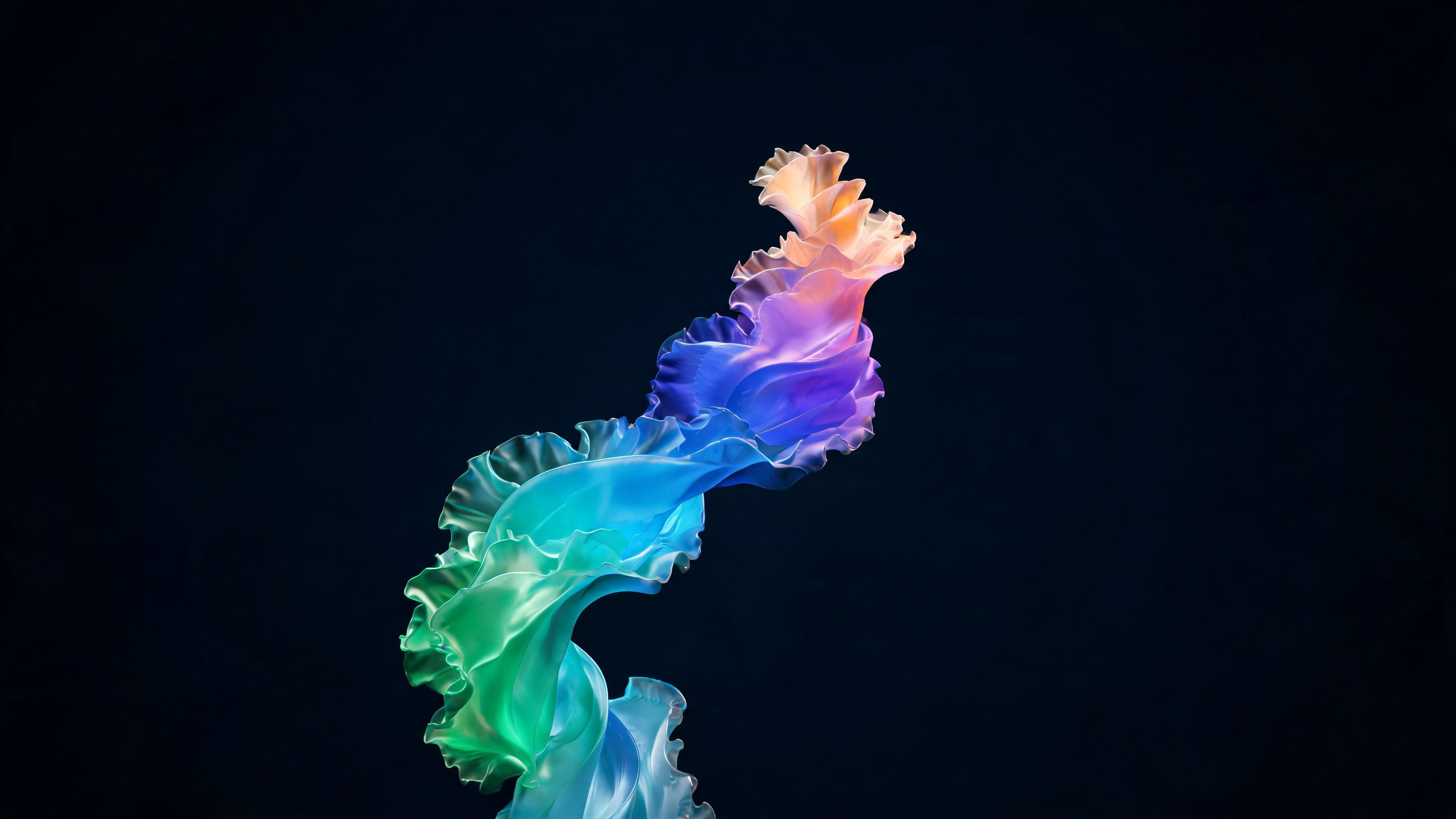 A single flowing ribbon of translucent, ruffled silk twists upward in a smooth S-curve, shifting through a full spectrum from emerald and turquoise at the base to sapphire, violet, and peach near the tip. The vibrant, luminous colors glow against a deep midnight background, creating an airy, dreamlike mood.